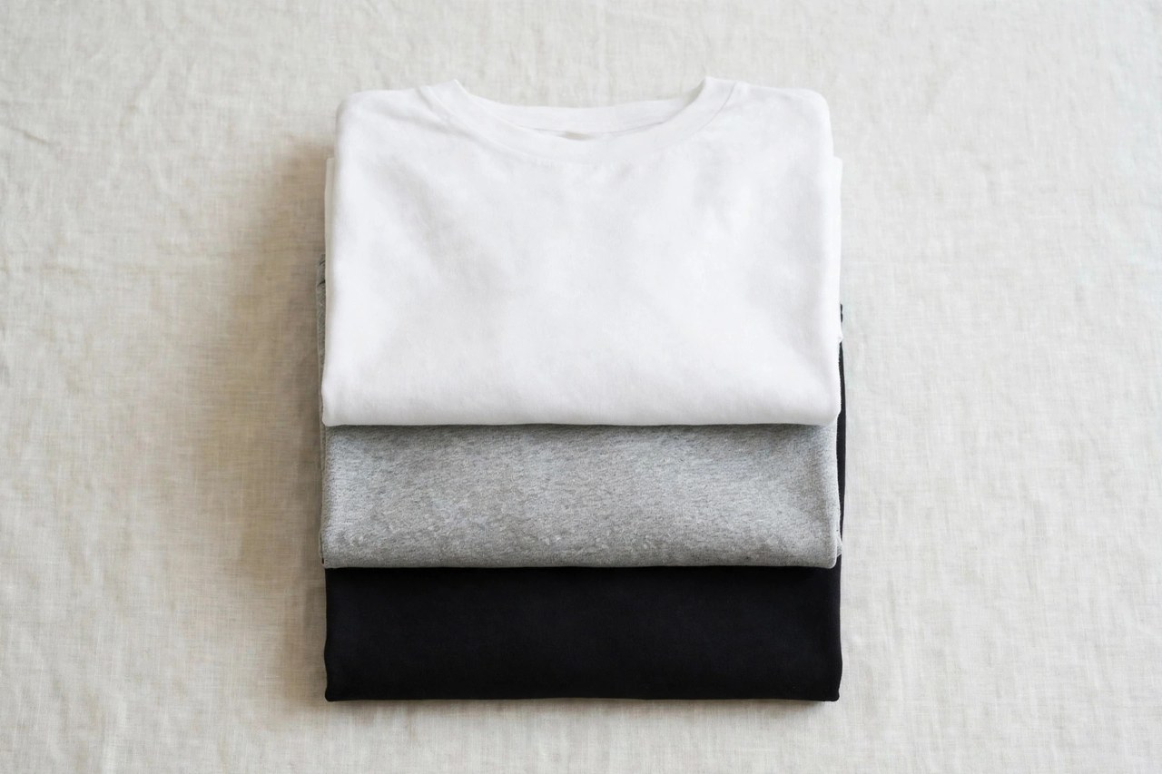 A flat lay of men's blank t-shirts in white, black and heather grey folded in a stack, product photography with no people