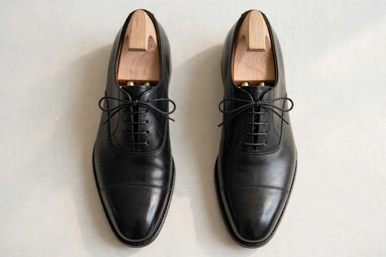 A flat lay of men's black leather Oxford dress shoes with shoe trees, product photography with no people