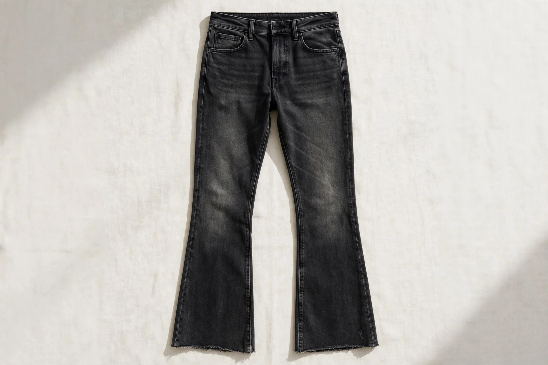 Men's kick-flare jeans in washed black denim laid flat, showing the slim leg flaring slightly from the knee to a cropped hem, product photography with no people