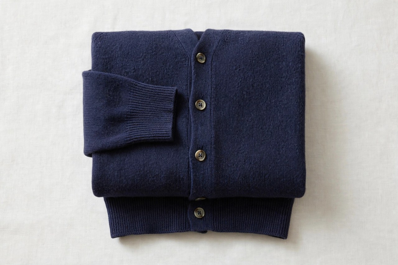 A flat lay of a men's merino wool cardigan in a fine knit with buttons, neatly folded, product photography with no people