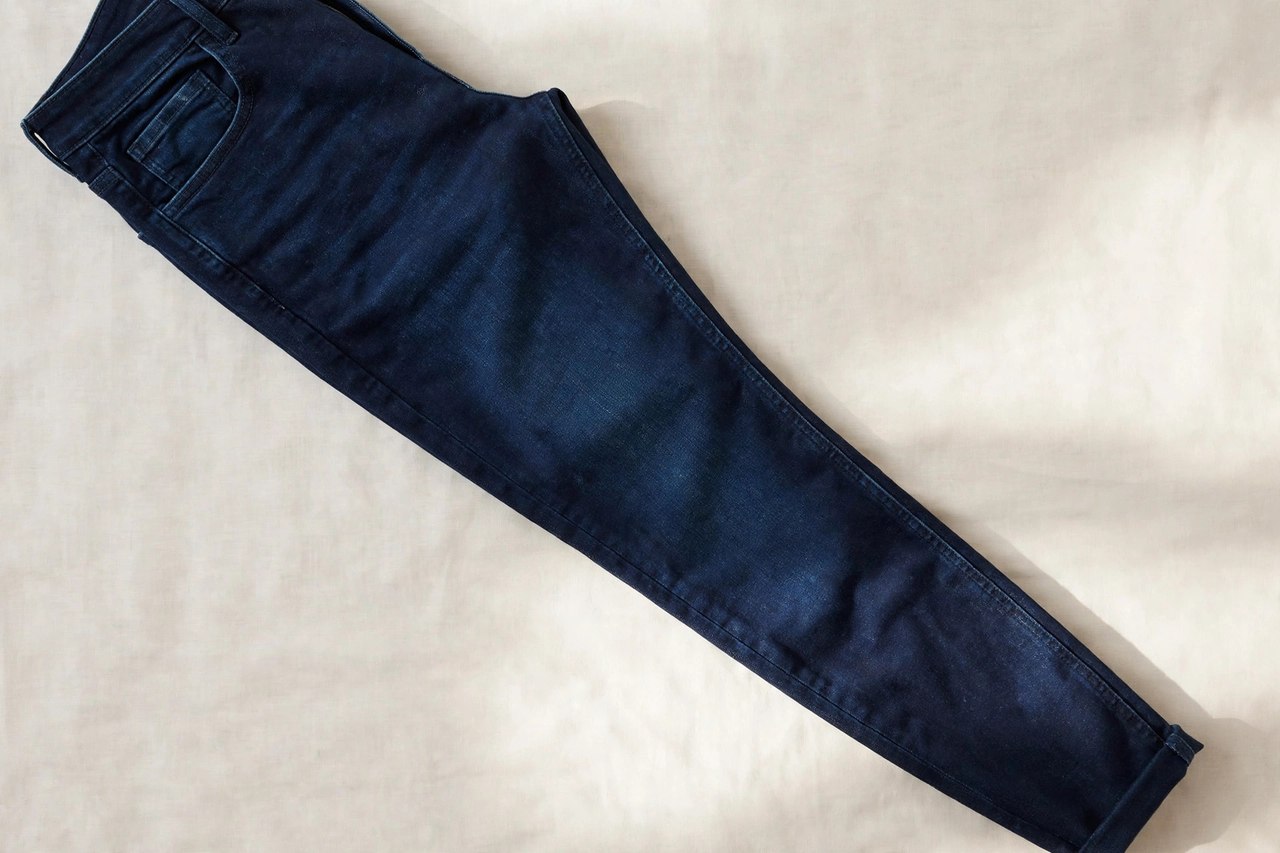Men's slim fit jeans in deep indigo laid flat, showing the close thigh and tapered leg, product photography with no people