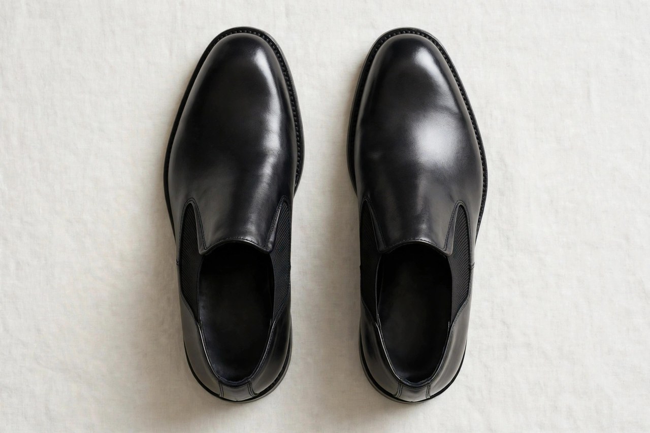 A flat lay of a pair of men's polished black leather slip-on dress shoes with elastic side gores, product photography with no people