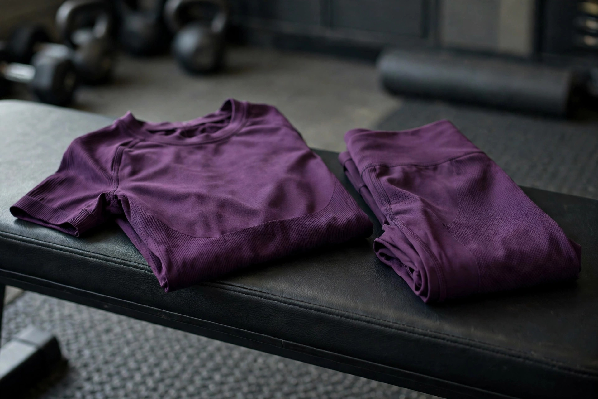 Women's performance workout clothing, a sweat-wicking training top and compression leggings folded on a gym bench