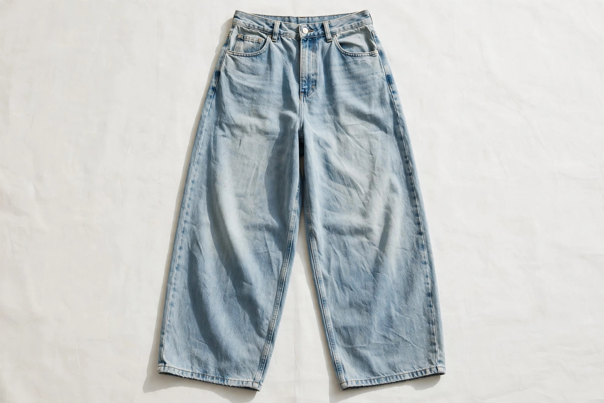 Women's baggy jeans in faded light-blue denim laid flat, showing the loose, wide leg falling straight from hip to a full-length hem, product photography with no people