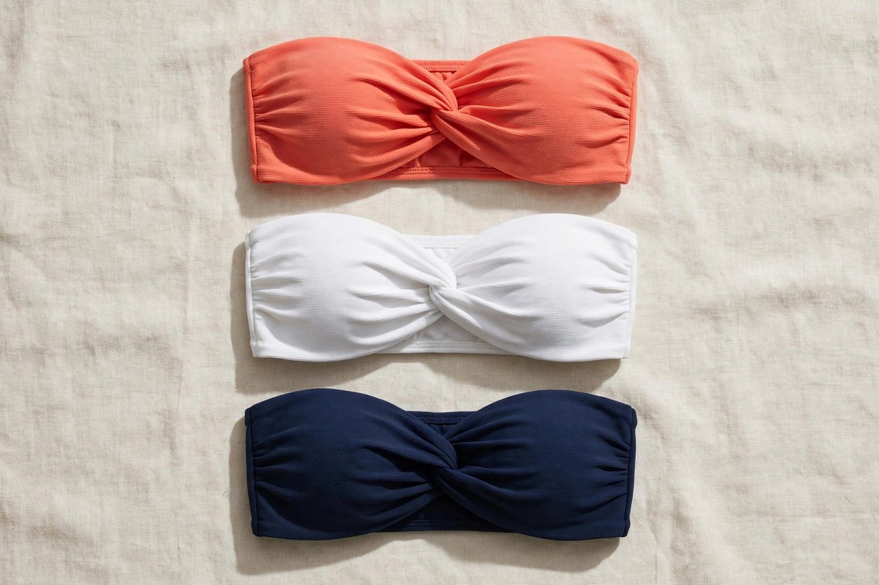 Women's bandeau swimsuits in strapless twist-front styles in coral, white, and navy, flat lay