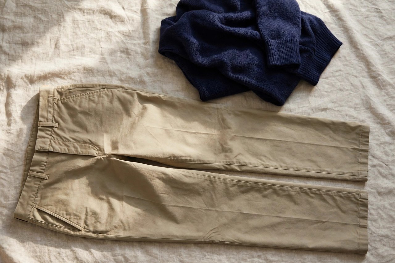 A pair of women's khaki business casual chino pants with a straight leg folded with a navy knit top