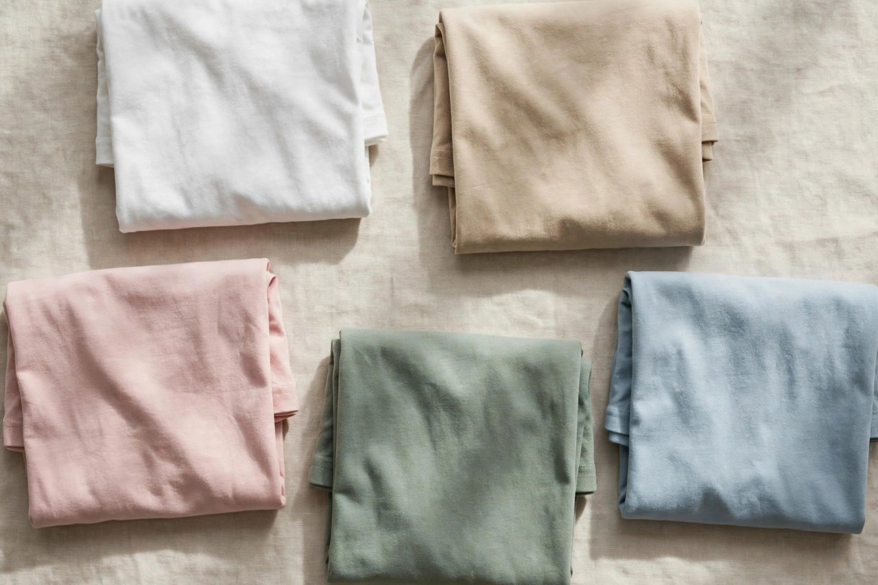 Folded womens fashion cotton tees in blush, sage and cream with soft drapey folds on a neutral background