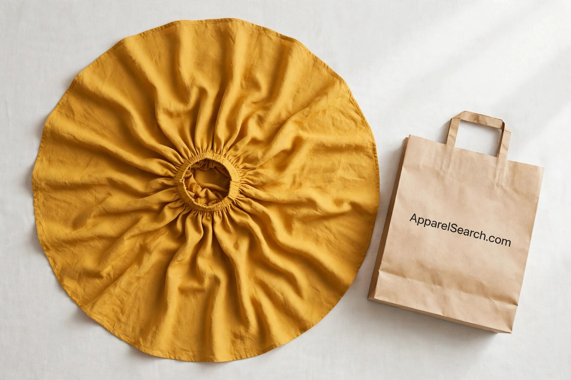 Women's circle skirt in mustard yellow fabric spread flat in a full circle showing the rippling folds from the small centre waistband, a paper shopping bag printed ApparelSearch.com beside it, product photography with no people