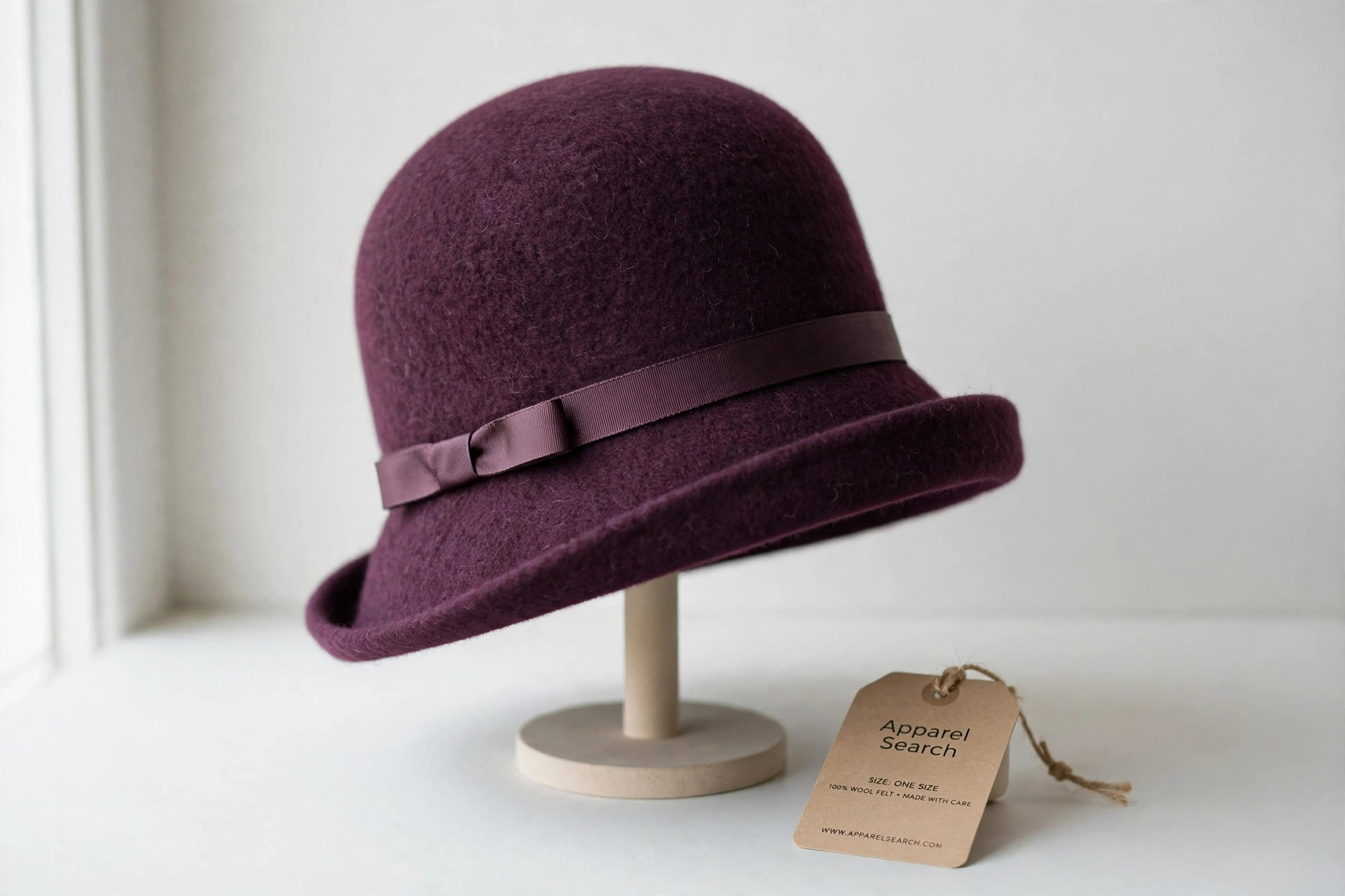 Women's cloche hat in deep plum wool felt with a ribbon trim on a plain display stand against a clean light background, product photography with no people