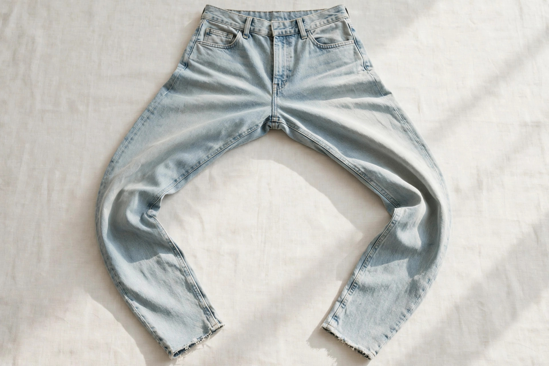 Women's horseshoe jeans in a pale stonewashed denim laid flat, showing the pronounced inverted-U curve of the leg from hip to tapered ankle, product photography with no people