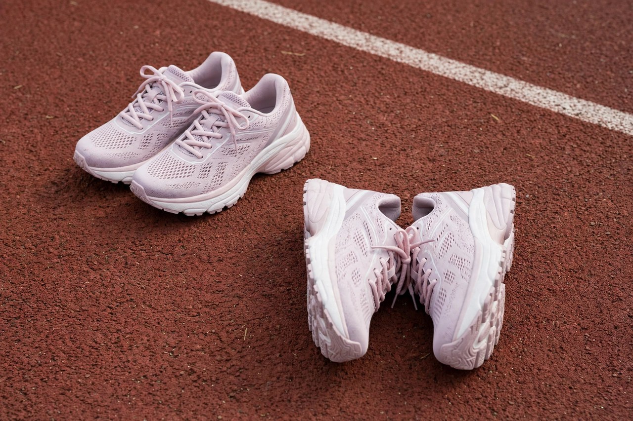 A pair of women's jogging sneakers with cushioned soles beside a second rotated pair, on a running track background