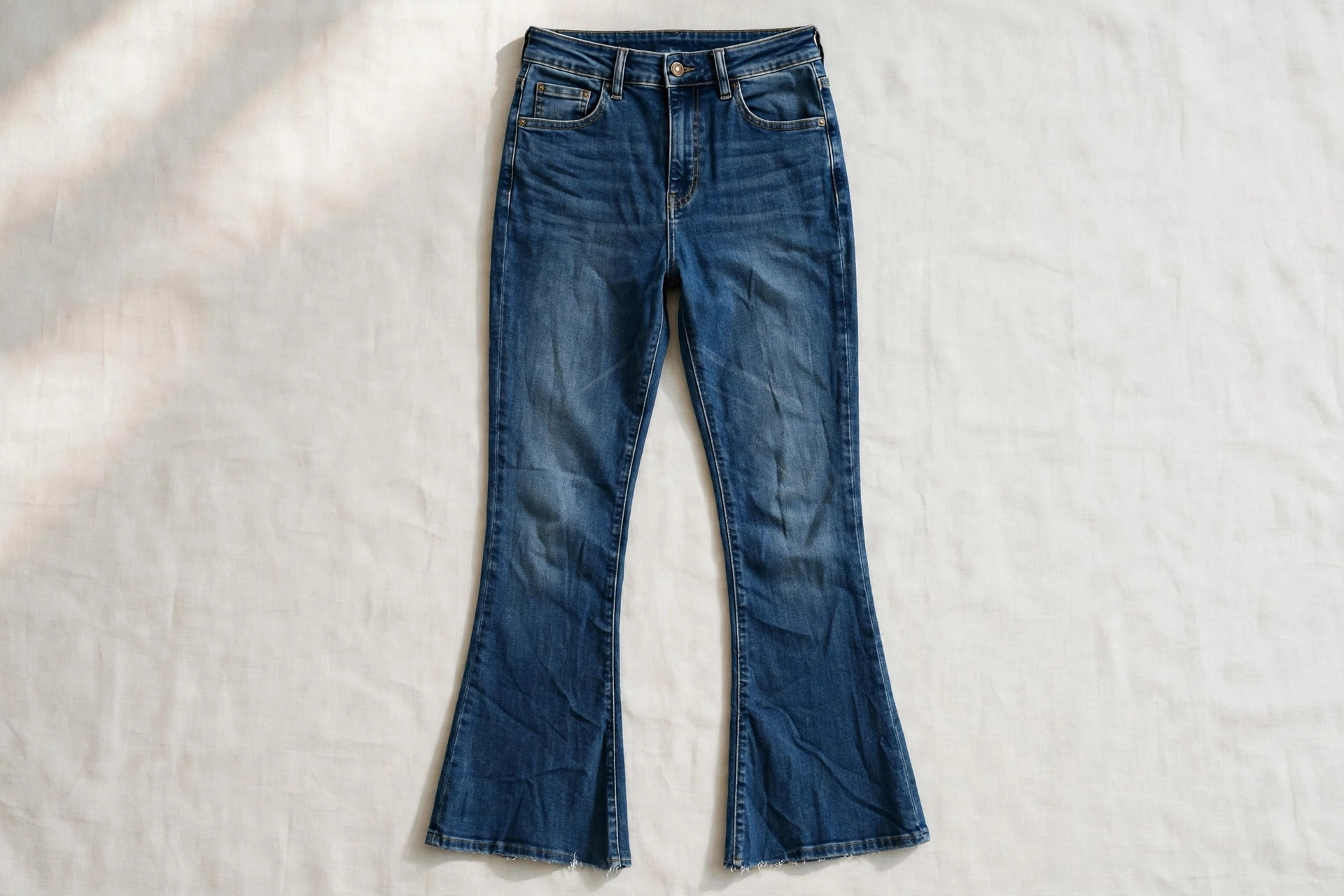 Women's kick-flare jeans in medium indigo denim laid flat, showing the slim leg opening into a short flare cropped above the ankle, product photography with no people