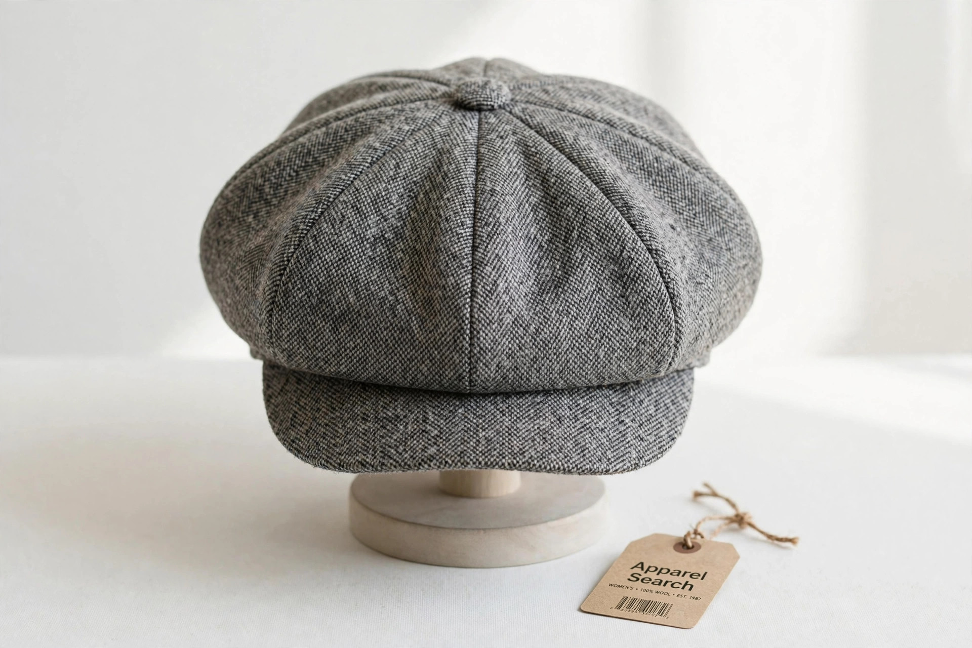 Women's newsboy cap in grey checked wool with a full eight-panel crown and centre button on a plain display stand against a clean light background, product photography with no people