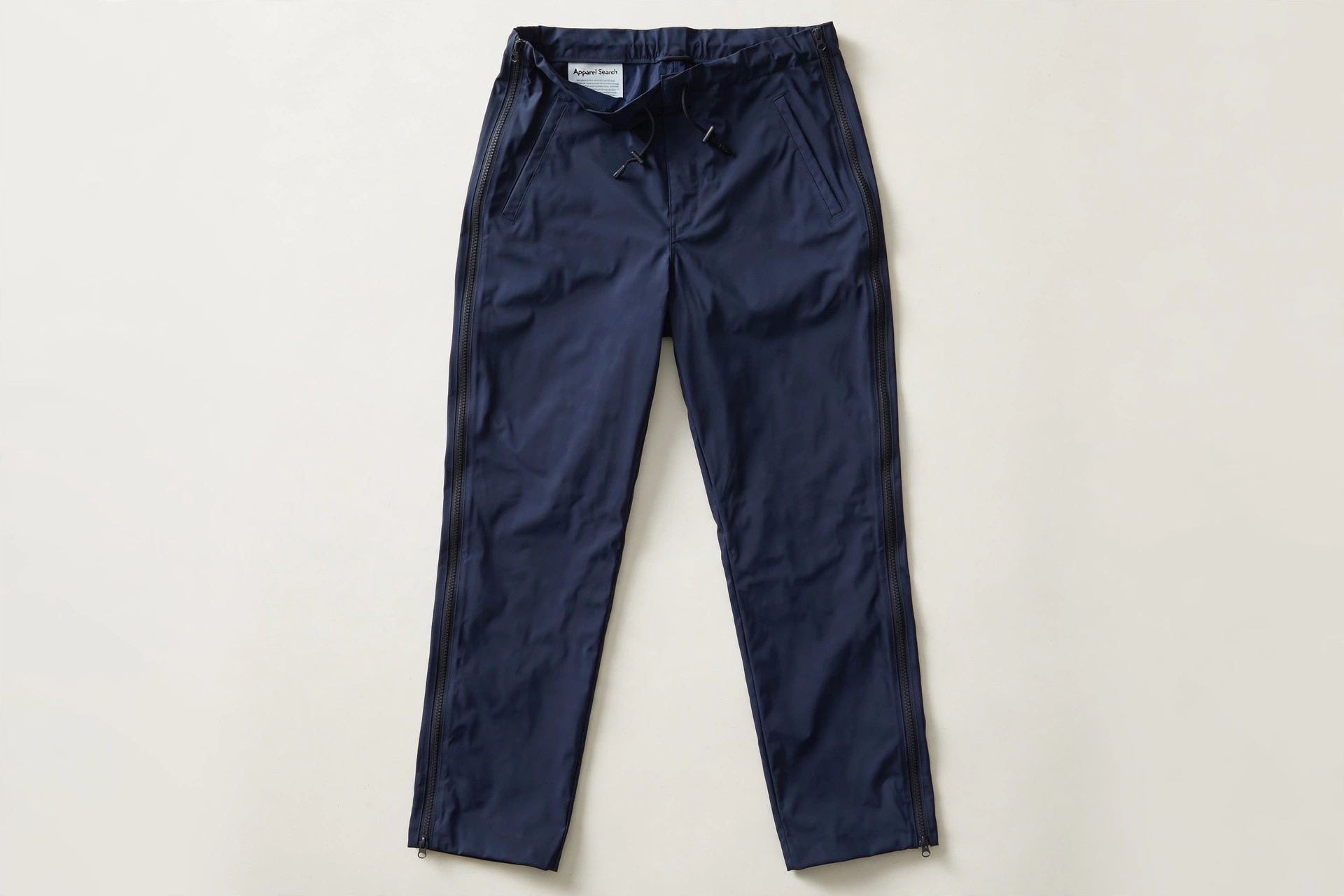 Women's rain pants in navy waterproof fabric with full-length side zips, laid flat, product photography with no people