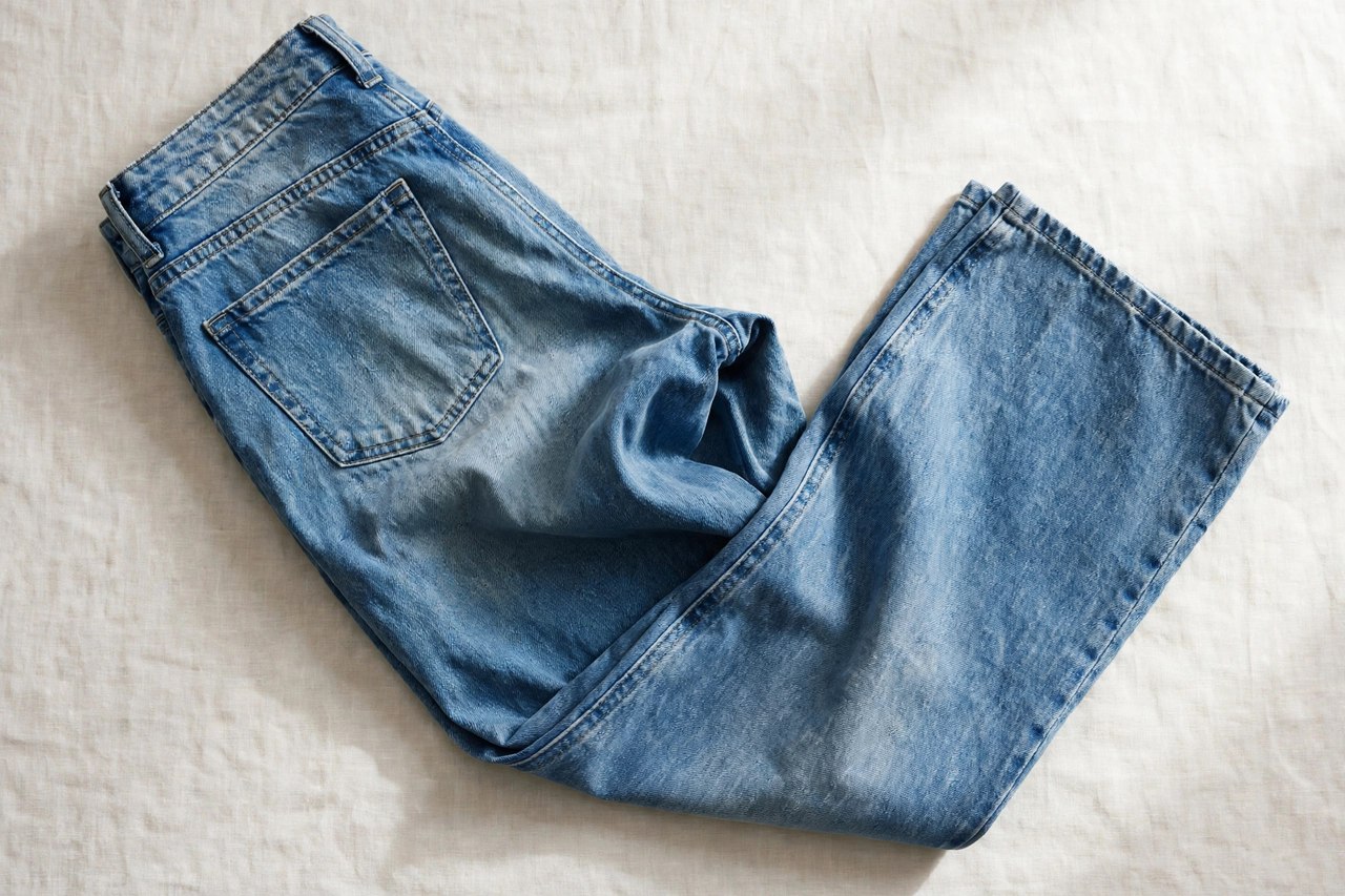 Women's relaxed fit jeans in a mid-blue wash folded loosely to show the easy seat and thigh, product photography with no people