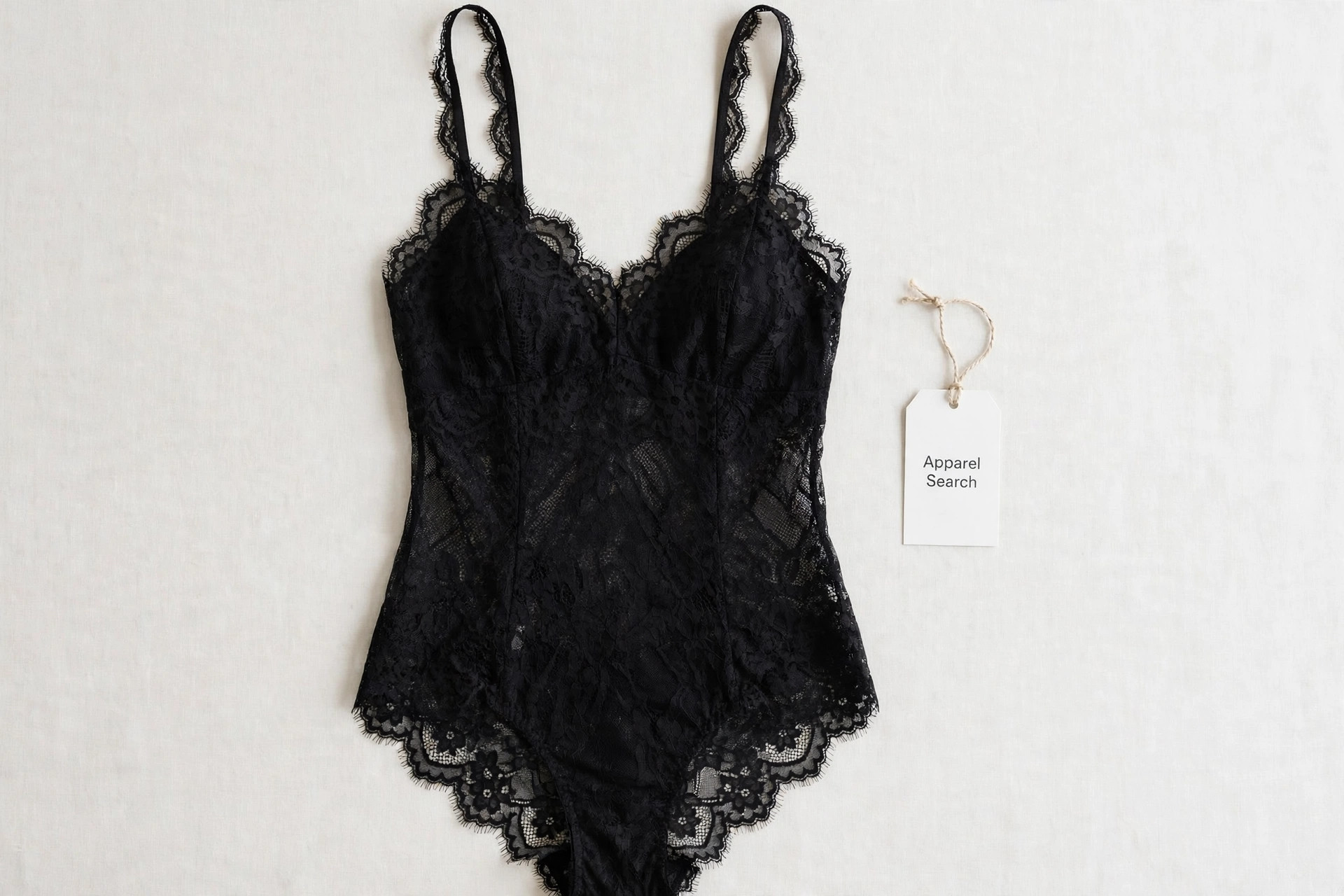 Women's teddy lingerie garment in black lace, a one-piece camisole top joined to a panty bottom, laid flat with thin straps neatly arranged, flat-lay product photography with no people