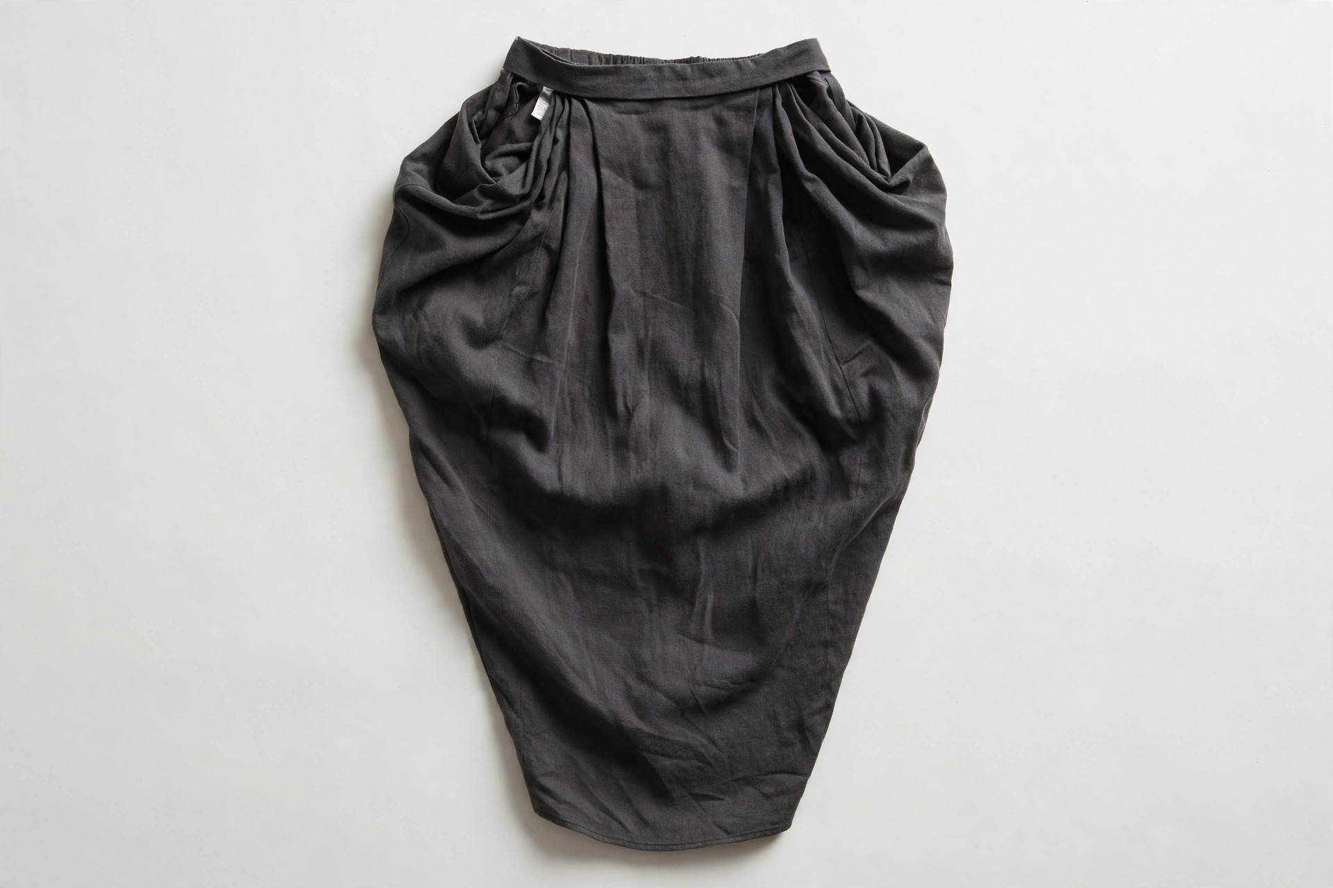 Women's tulip skirt in charcoal fabric laid flat, showing the fullness gathered at the hip tapering down to a narrow hem, product photography with no people