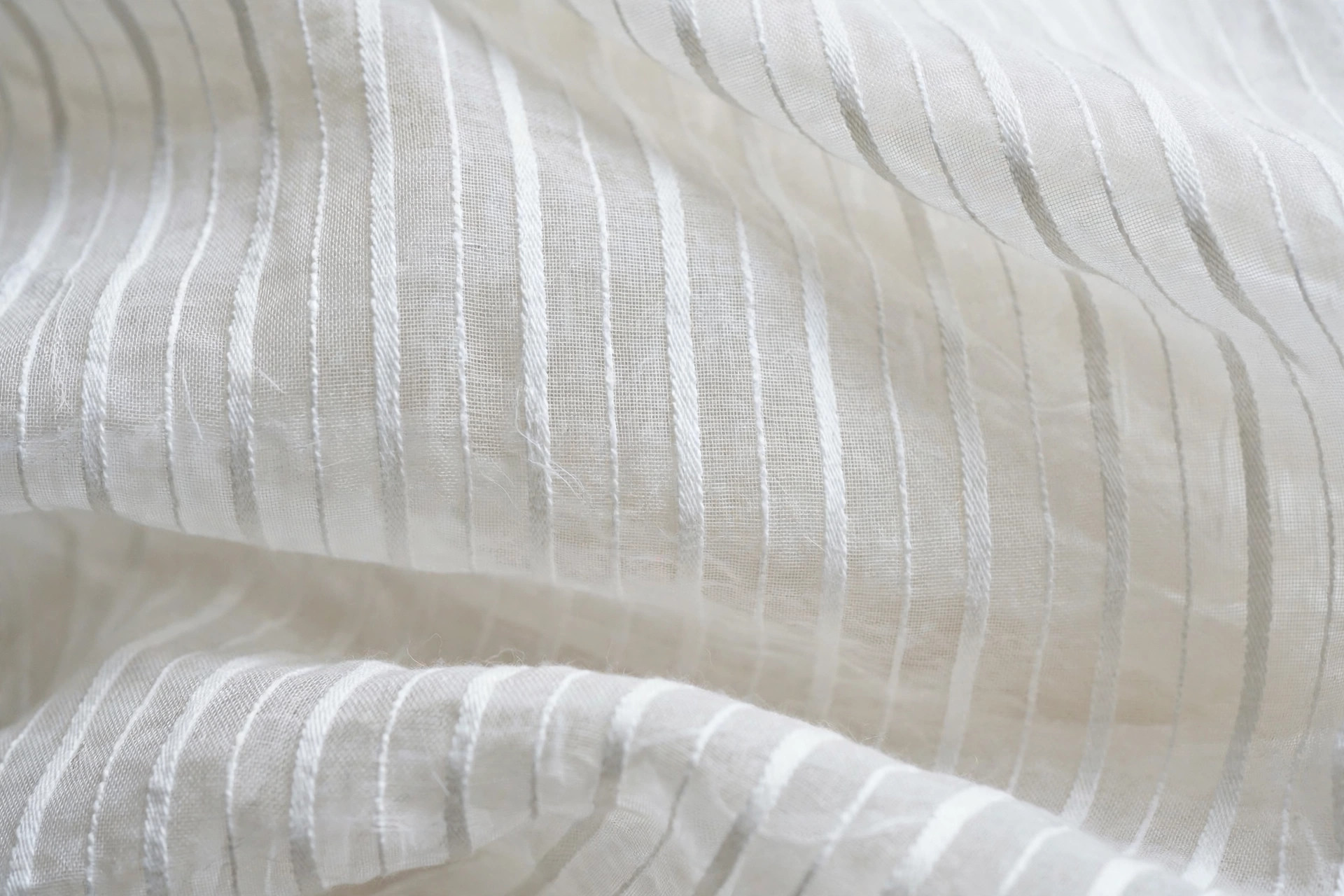 Sheer white dimity cotton fabric with fine corded stripes, delicate textile close-up