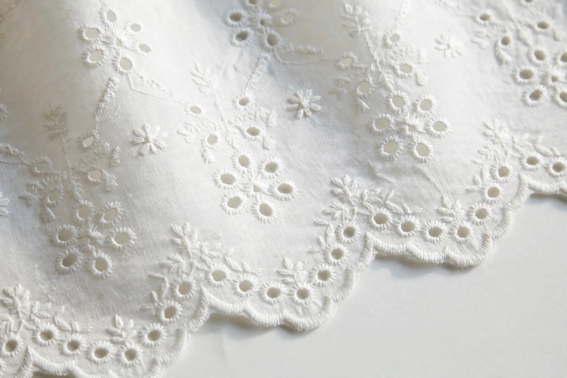 White eyelet cotton fabric with embroidered holes and scalloped floral cutwork pattern