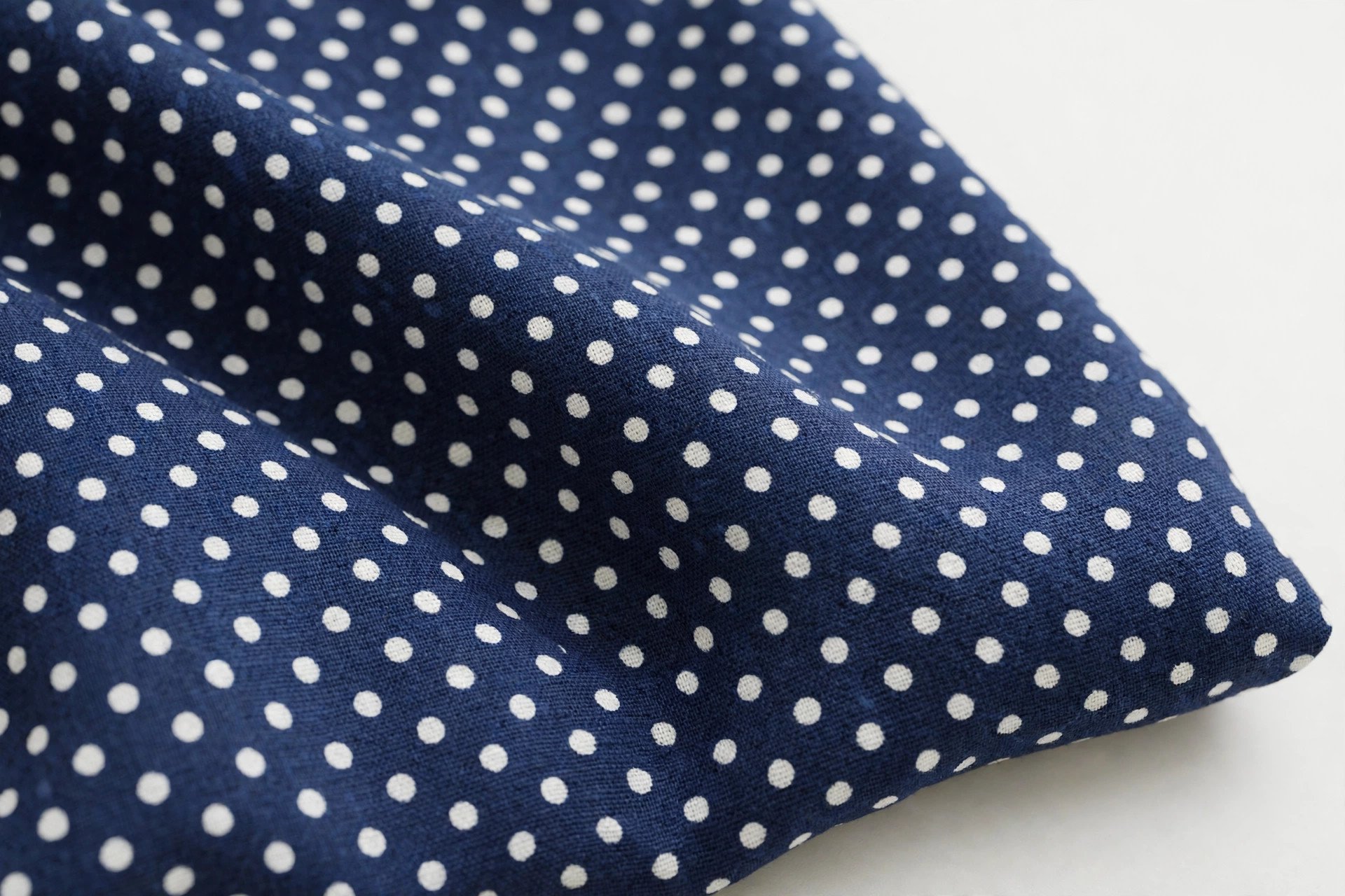Polka dot fabric with evenly spaced white round dots on navy ground