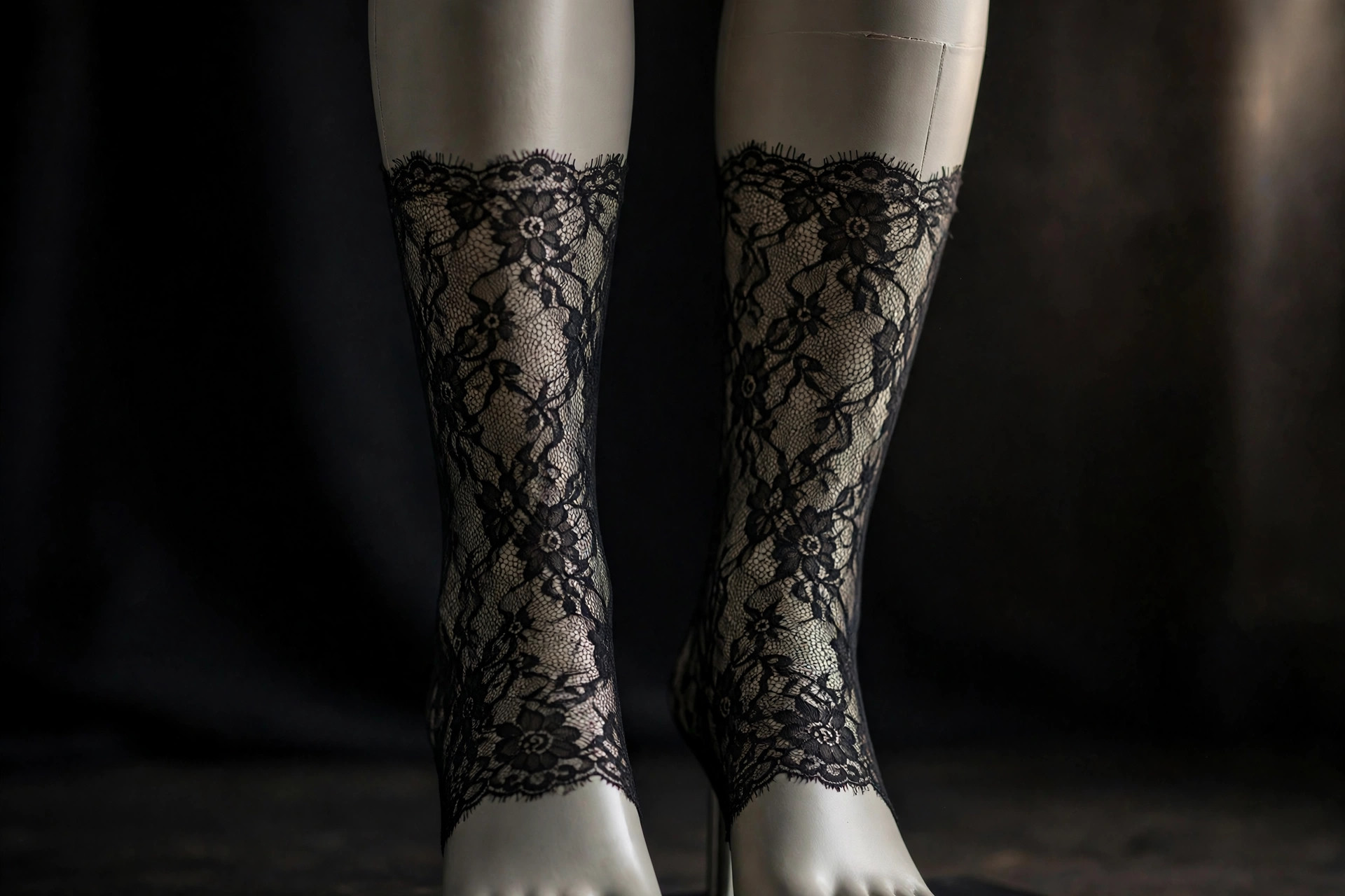 Black lace-patterned tights with floral design on mannequin legs in soft studio light