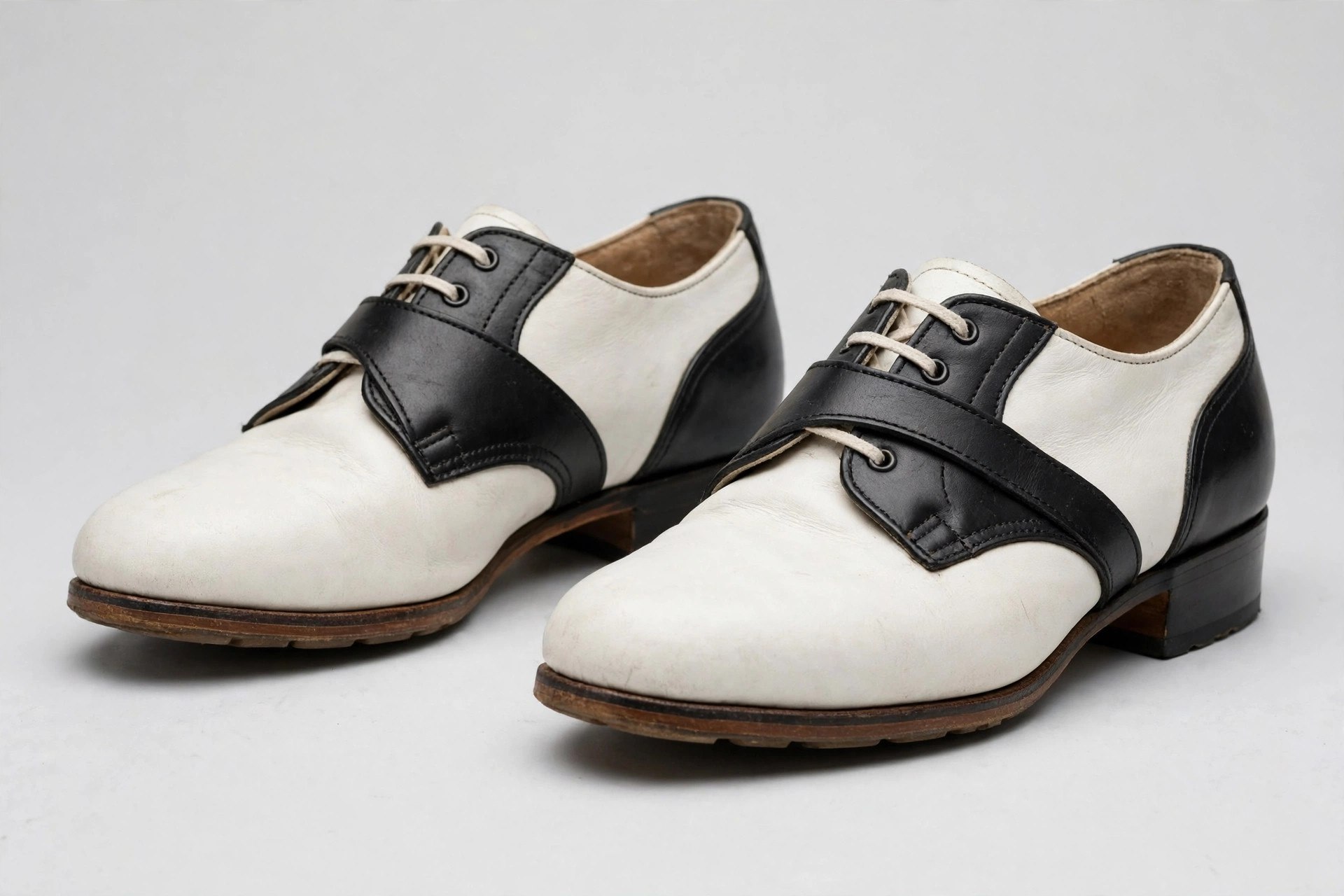 A pair of classic white leather saddle shoes with a dark brown saddle panel across the instep and brick-red rubber soles.