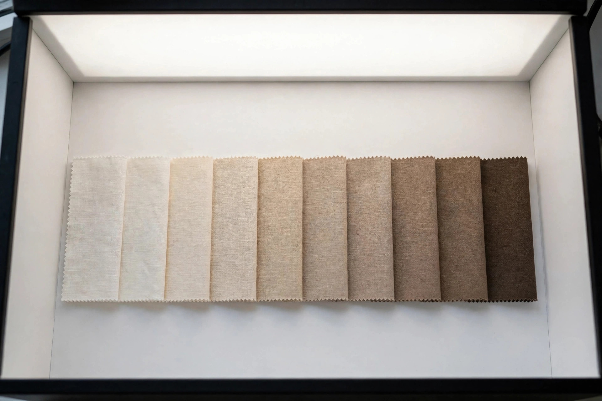 Row of fabric swatches in slightly different shades arranged as an approved shade band under a light box