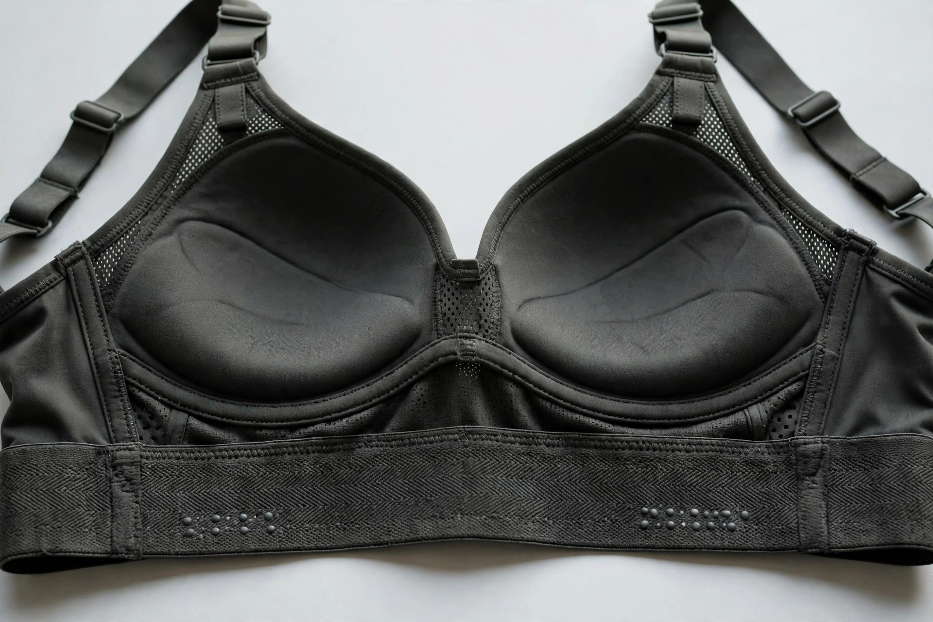 Close-up of a high-support sports bra's wide elastic underband, molded cups and adjustable straps laid flat on a studio background
