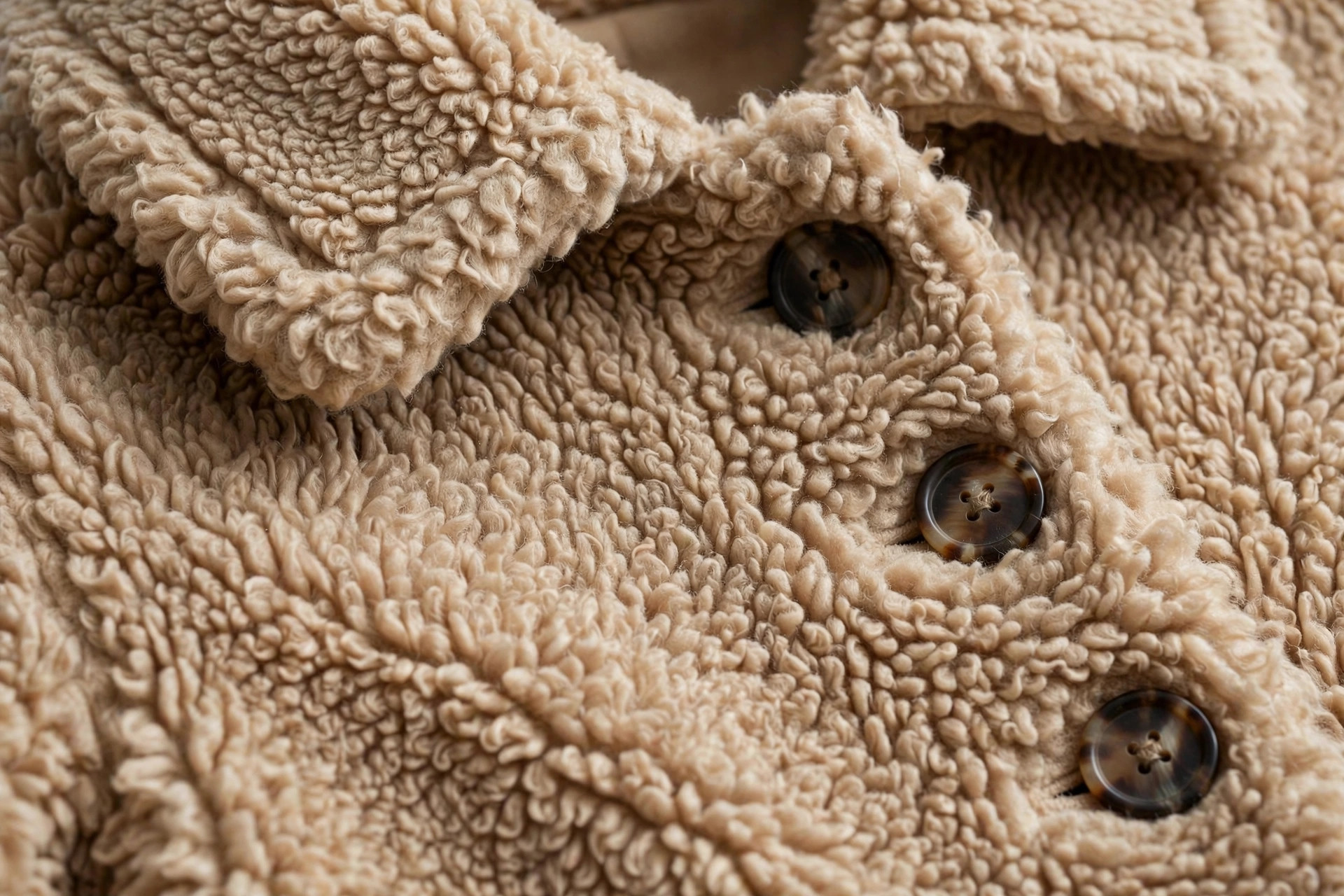 Close-up of deep camel teddy pile fabric showing the curly texture, collar, and buttons of a coat