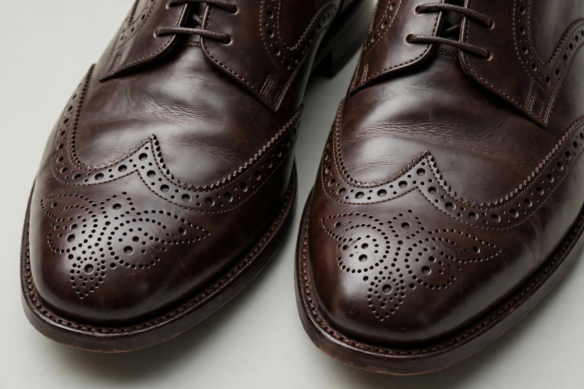 A pair of tan leather wingtip brogue shoes showing the wing-shaped toe cap and perforated medallion, worn with cuffed tweed trousers.