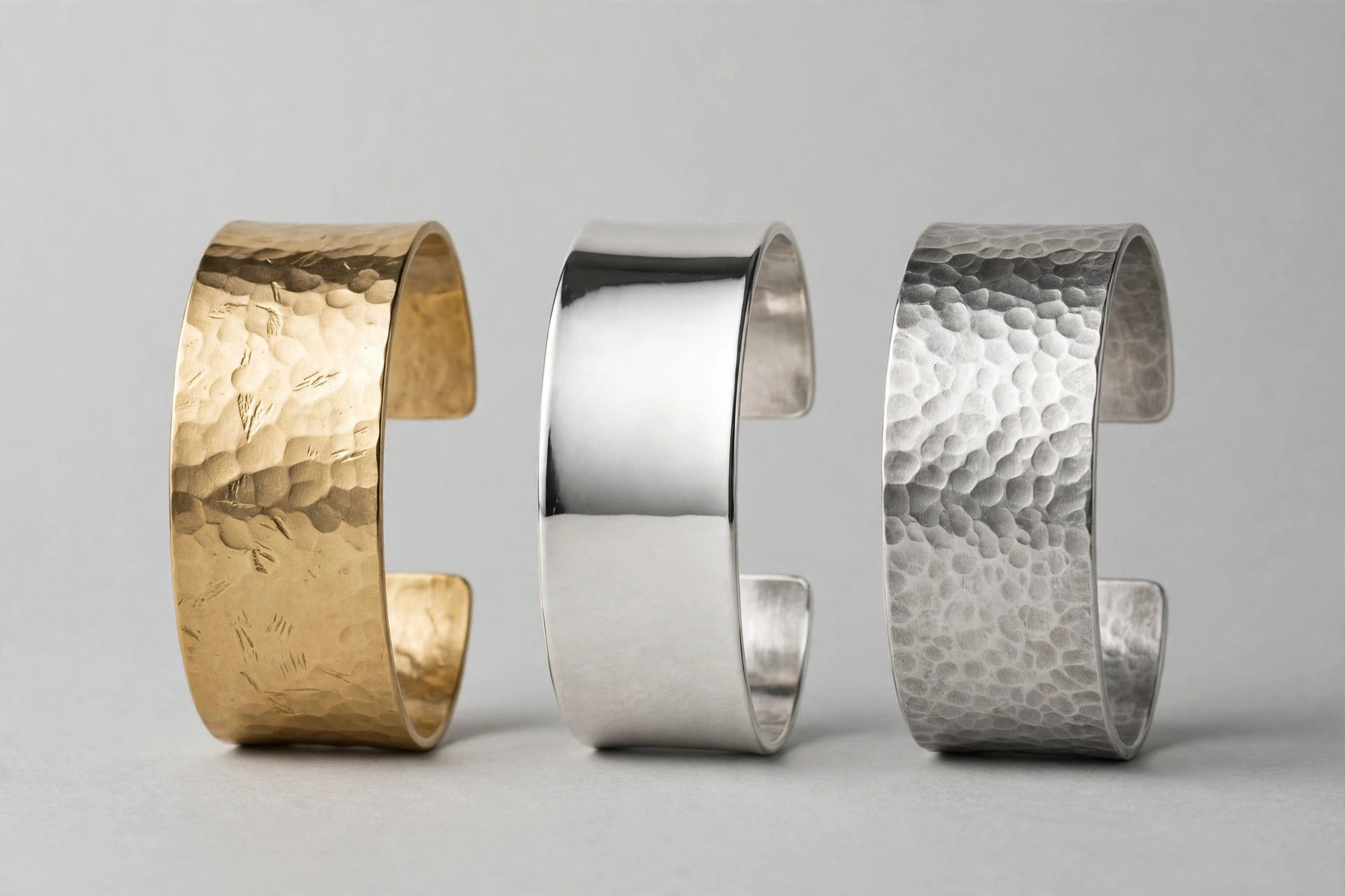 Wide metal cuff bracelets in gold, silver and hammered finishes standing on a studio background