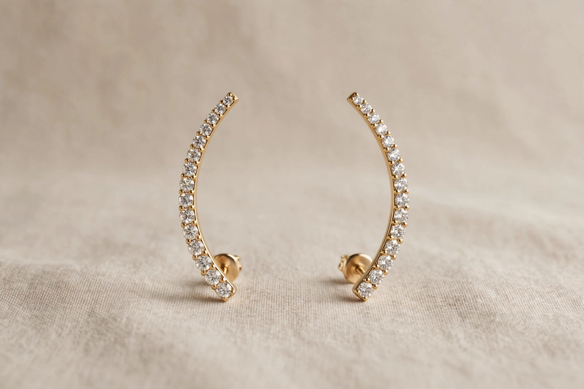 Pair of curved ear climber earrings with crystals sweeping upward on a neutral backdrop