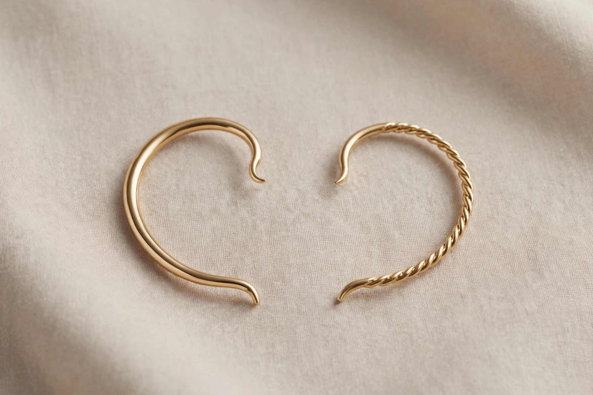 Pair of curved gold ear cuff bands for the edge of the ear on a neutral backdrop