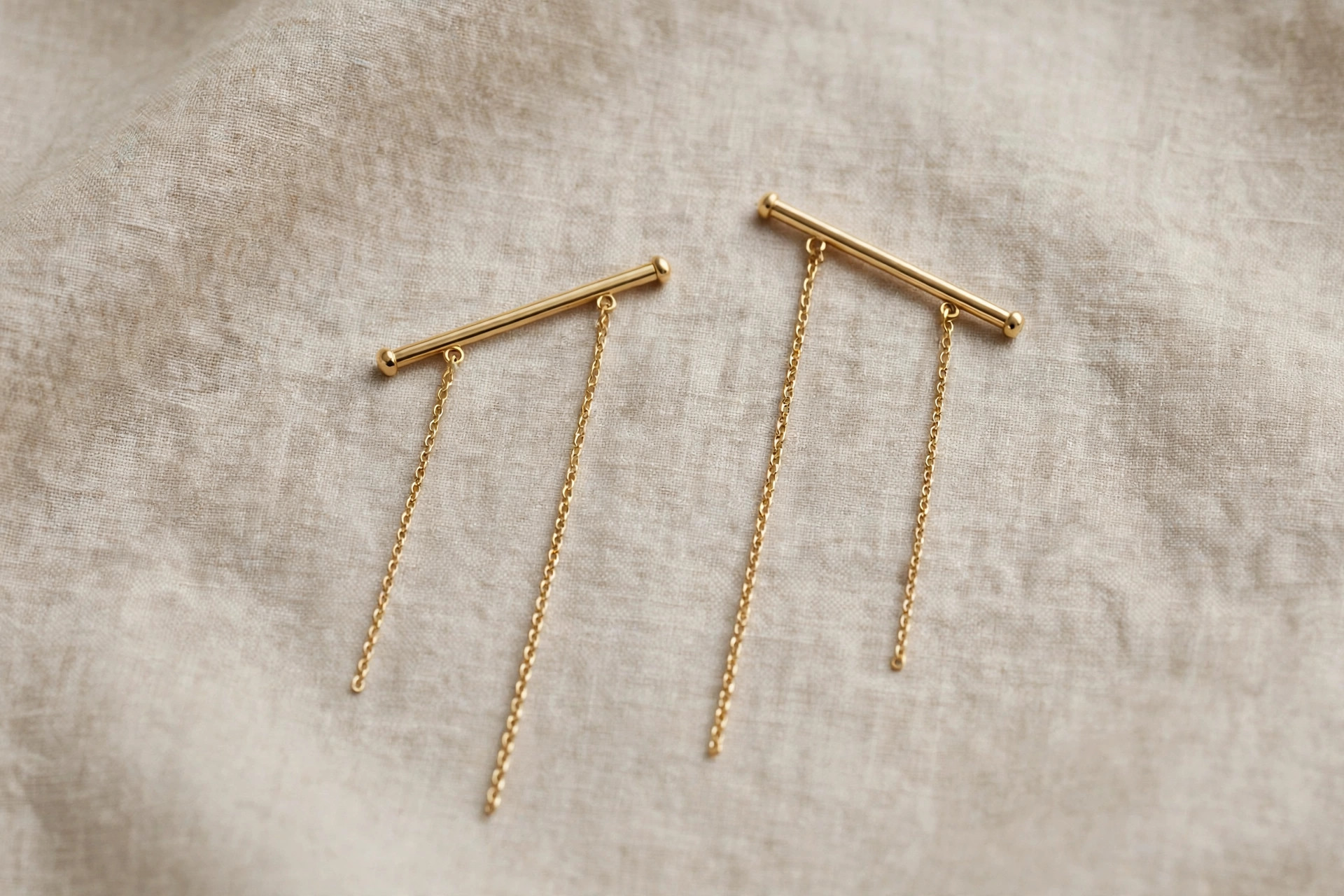 Pair of fine gold threader earrings with slender bar ends on a neutral backdrop