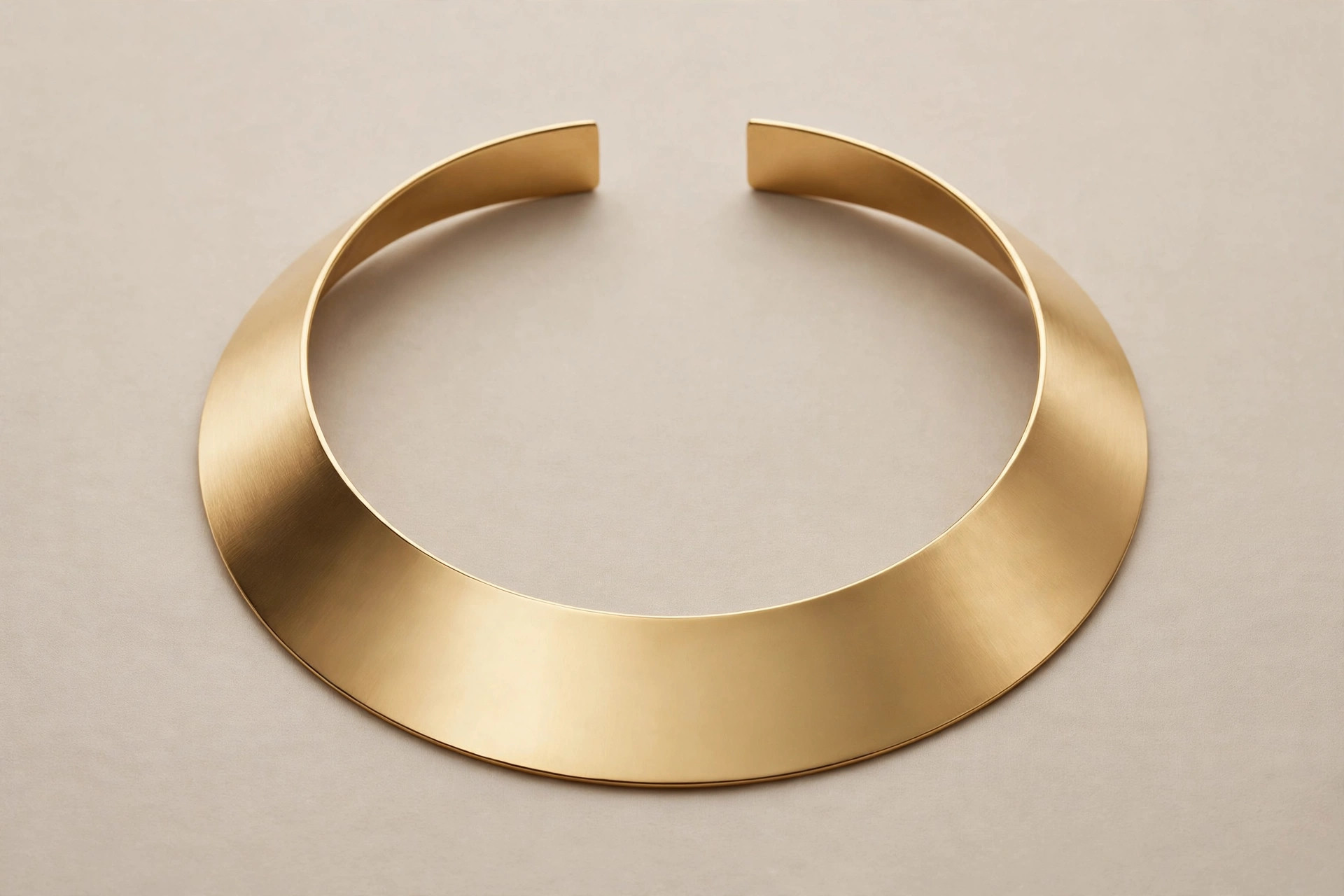 Wide flat gold collar necklace displayed on a neutral backdrop