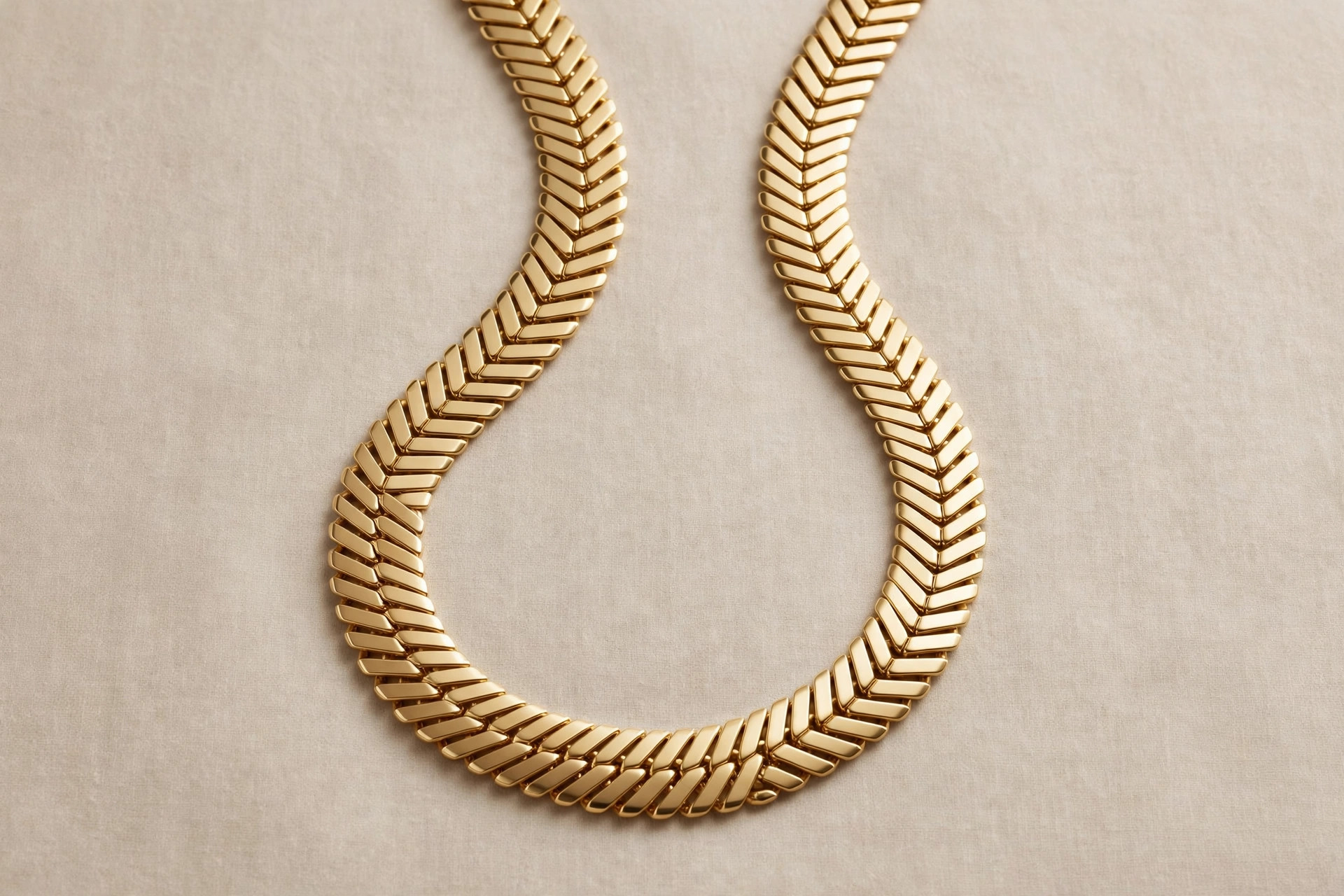 Flat gold herringbone chain necklace with a smooth liquid-metal shine on a neutral backdrop