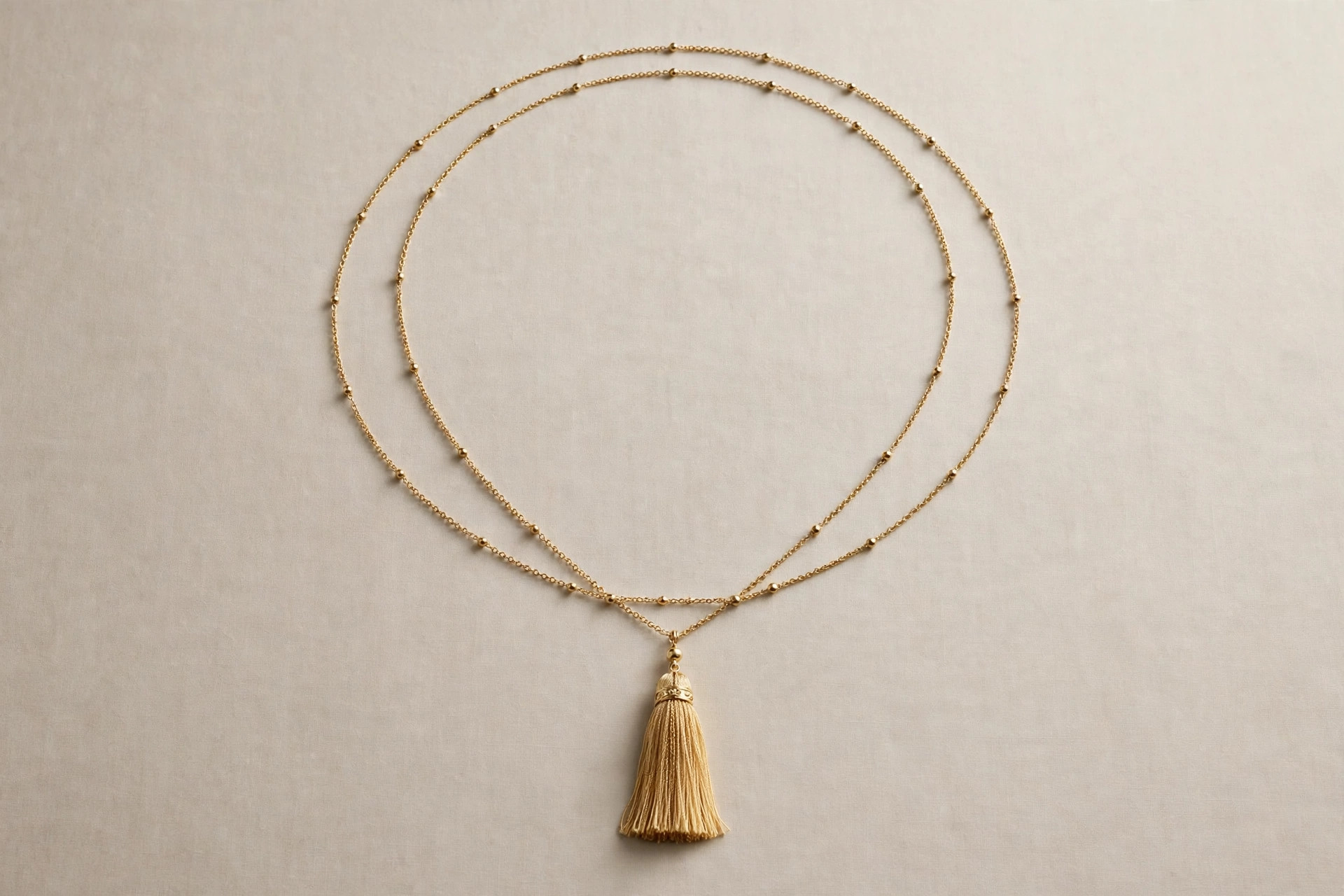 Very long sautoir necklace with a tassel pendant displayed in a long loop on a neutral backdrop