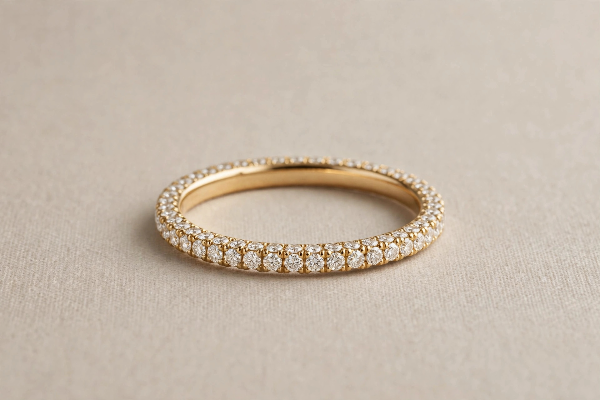 Gold eternity ring with a continuous circle of diamonds on a neutral backdrop